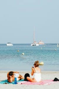 Rolig sandstrand med palmer, steiner og lavt bølgeskvulp i varmt tropisk kystlandskap.