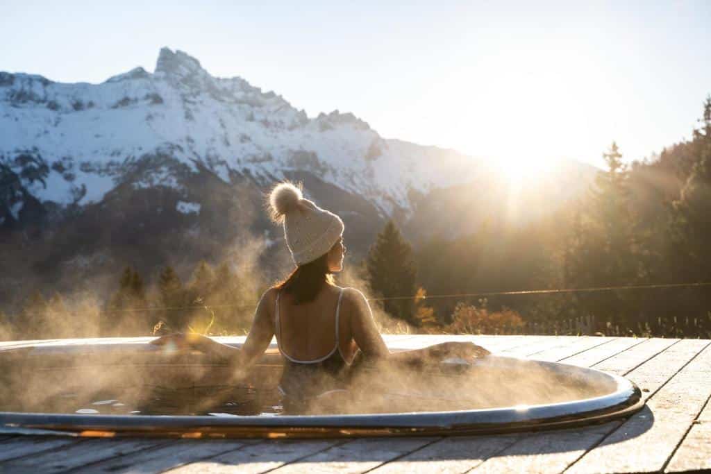 Utendørsbad hos Whitepod Eco-Luxury Hotel, stemningsfull kveld med solnedgang og utsikt over alpene