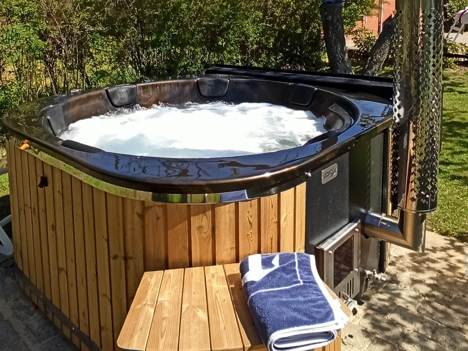 Vedfyrt badestamp med bobler og integrert ovn i hage – utendørs spa med massasjeeffekt og komfort.