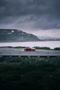 Bil på naturskjønn vei langs fjord og fjell i Norge – perfekt for en luksuriøs kjøretur gjennom norsk natur.