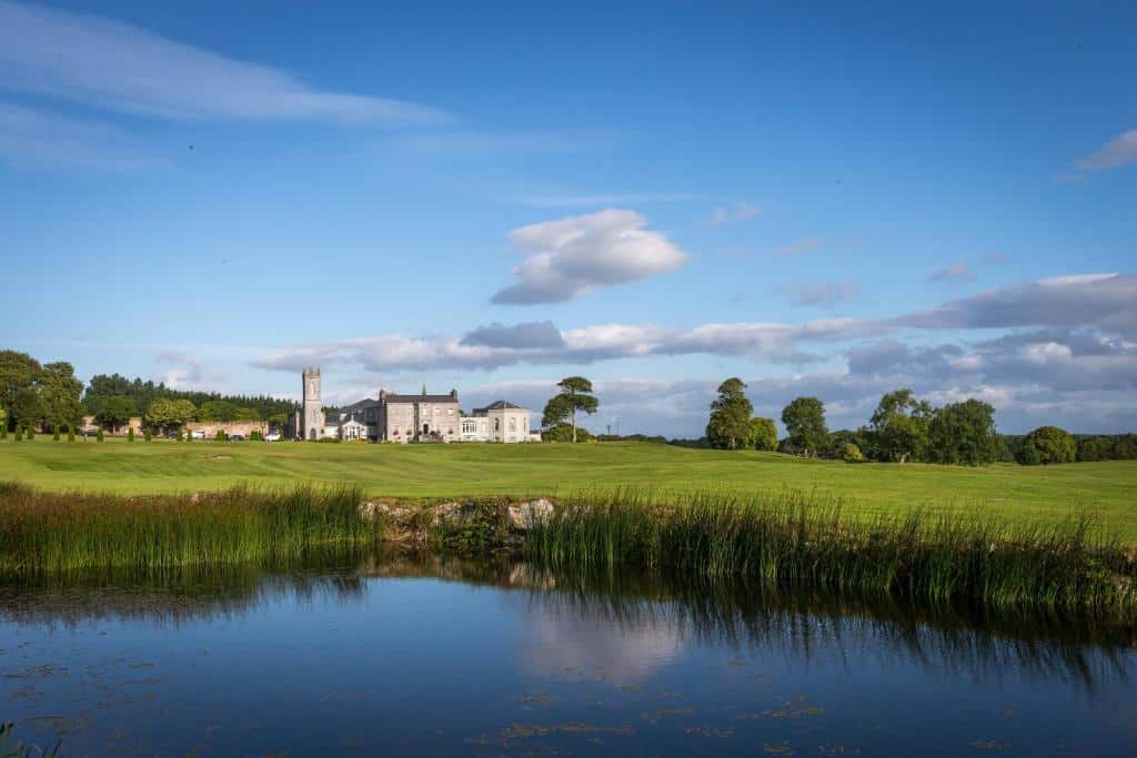 Glenlo Abbey ved innsjøen utenfor Galway, omgitt av grønne enger og rolig irsk landskap i ettermiddagslys.