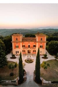 Hovedbygningen på Villa Lena i Toscana sett ovenfra i gyllent kveldslys – et historisk landsted omgitt av åser, skog og stillhet.
