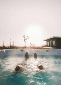 Person som slapper av i utendørs badestamp med utsikt mot solnedgang ved moderne hytte