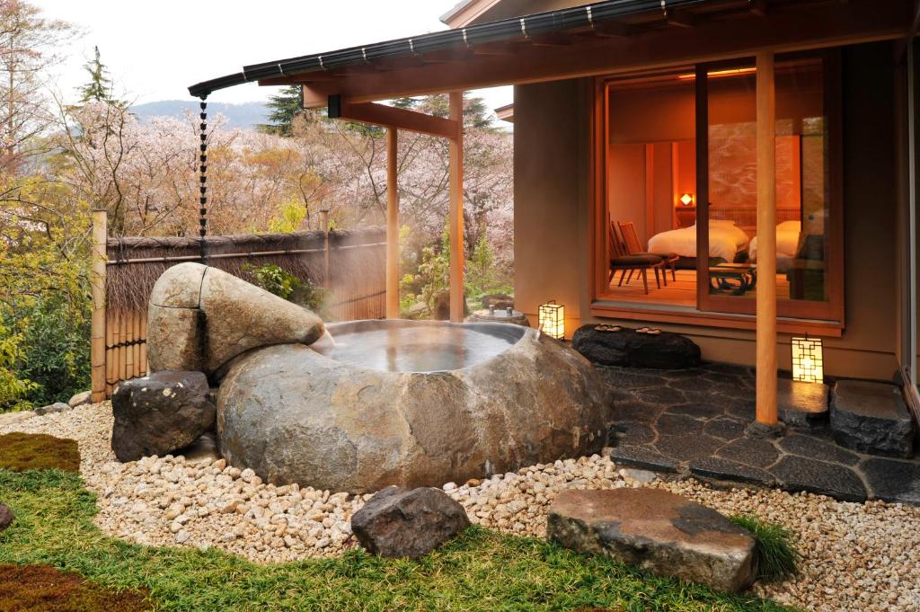 Privat utendørs onsen i naturstein ved tradisjonell ryokan i Hakone, omgitt av japansk hage og med utsikt mot rommet i varm kveldsbelysning.