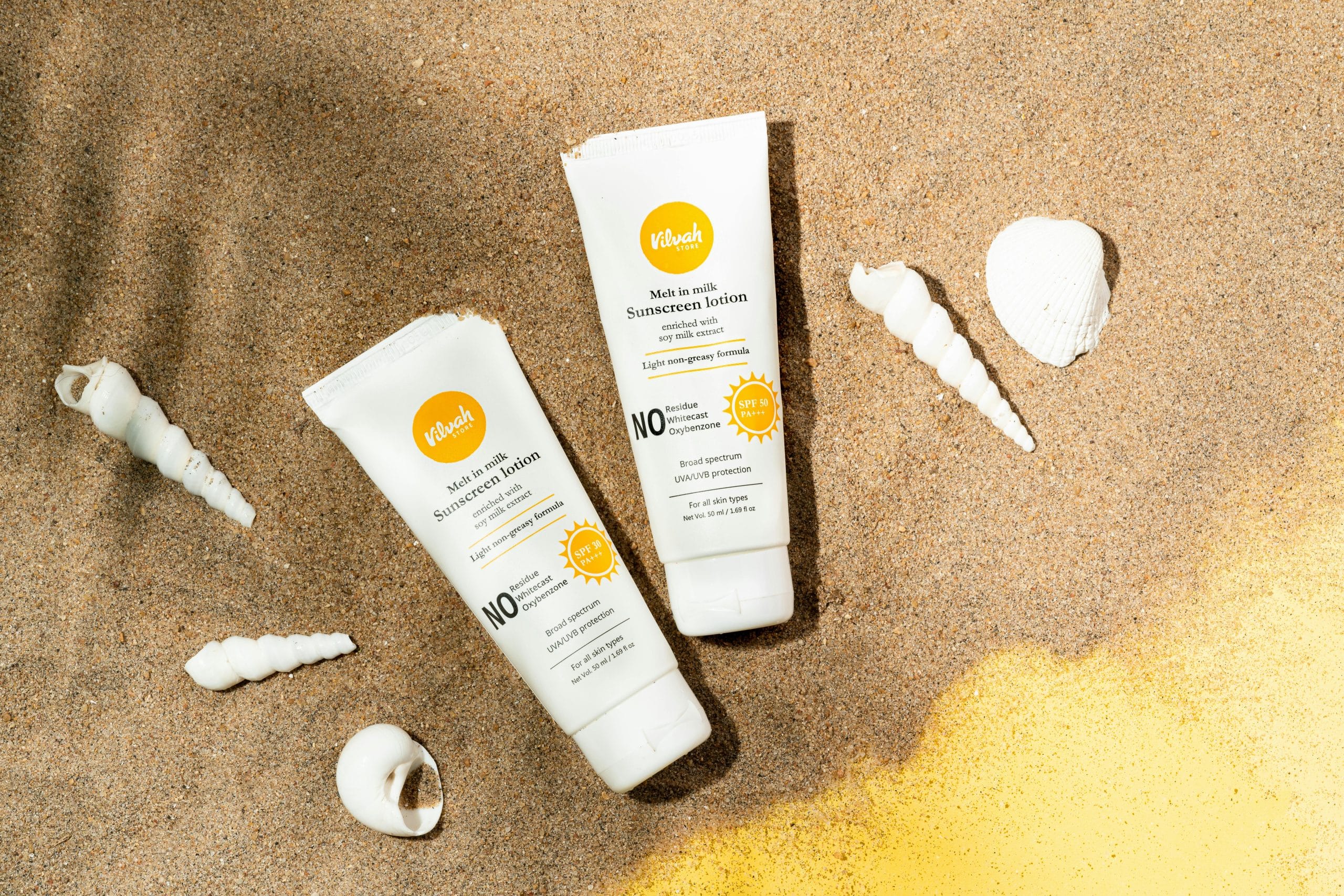 SPF sunscreen på sand med skjell – summer aesthetic strandbilde med solbeskyttelse for ferie ved Middelhavet.