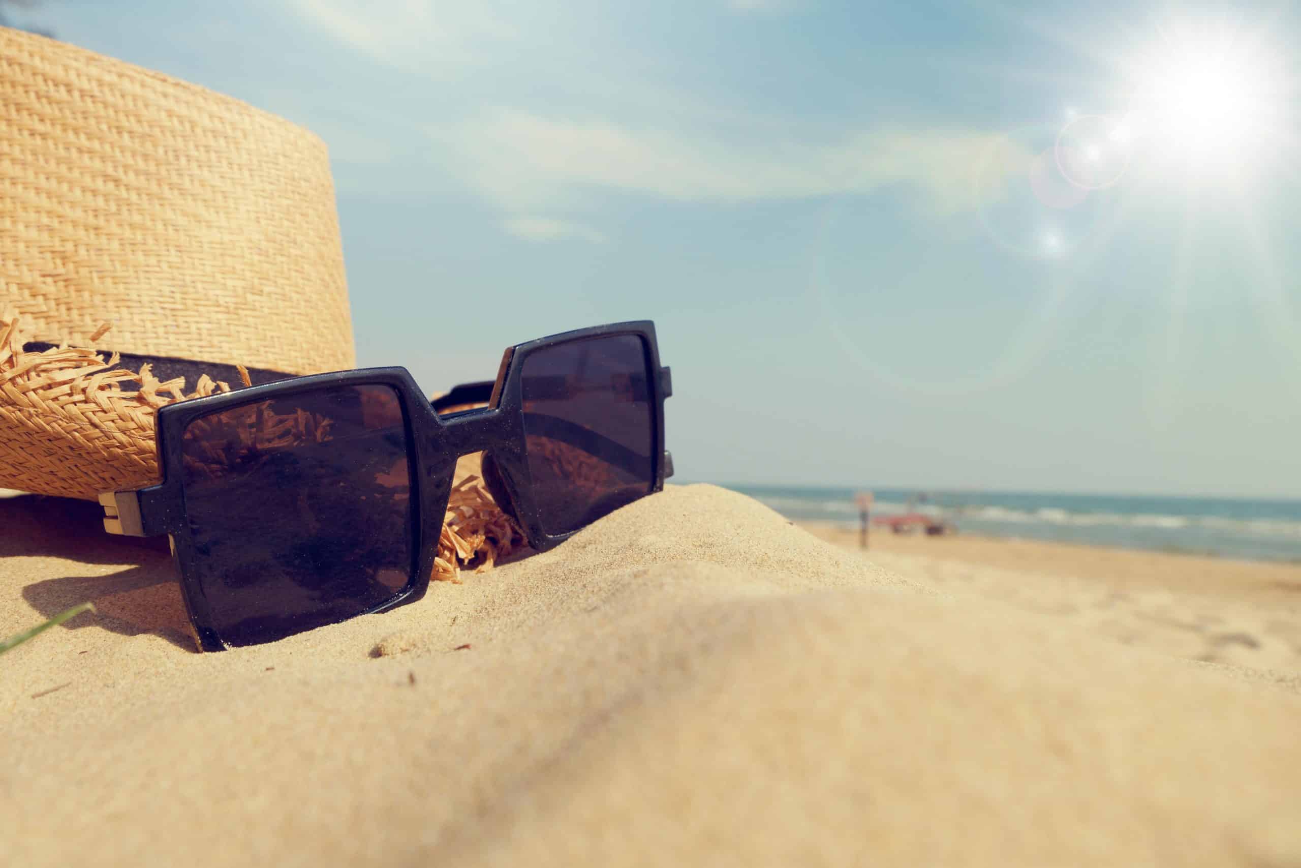Solbriller og stråhatt på sandstrand ved Middelhavet – sommerferie på Costa Blanca i Spania.