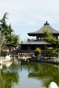 Tradisjonell japansk paviljong ved rolig dam med bro, grønne trær og klassisk hageanlegg i Japan.