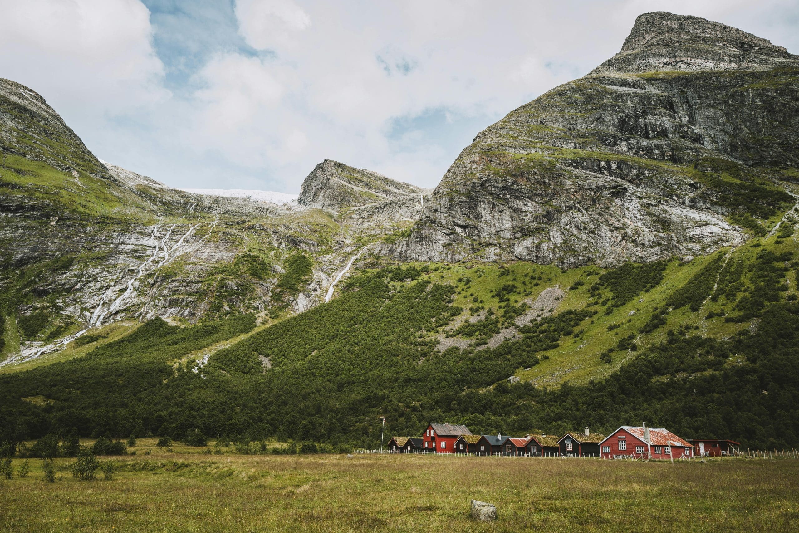 Tradisjonelle røde seterhus ved foten av dramatiske fjell i norsk fjordlandskap – naturskjønt område ideelt for sykkelferie og naturopplevelser i Norge.