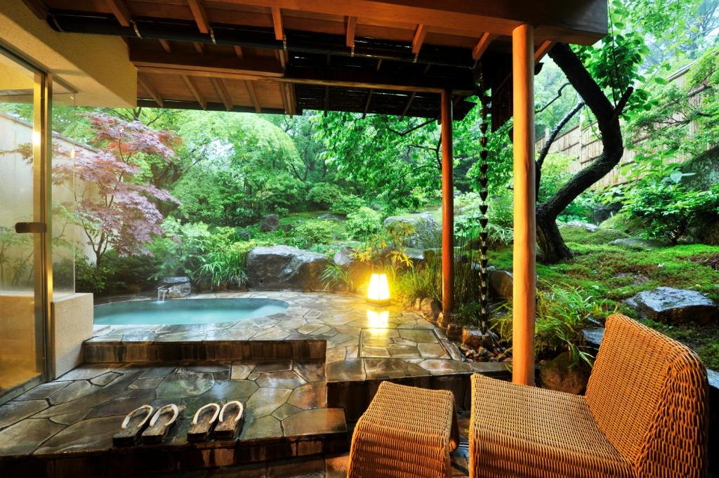 Utendørs onsen-bad i japansk hage med naturstein, grønn vegetasjon og tradisjonell ryokan-arkitektur.